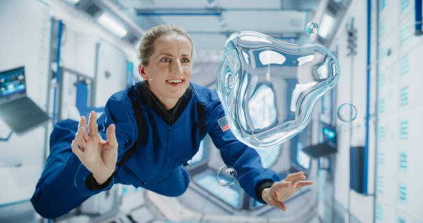 istock Female Astronaut in Blue Spacesuit Floating Inside Space Station, Interacting with Floating Water Bubble. Demonstrates Human Achievement in Space Exploration. Cosmos Encourages Scientific Discovery 2156520007