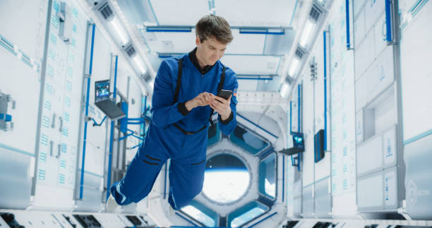 istock Cheerful Male Astronaut Floating in Zero Gravity Inside a Spaceship. Happy Caucasian Specialist Using Smartphone in Space, Checking News, and Communicating with Family or Friends Online. 2156520218