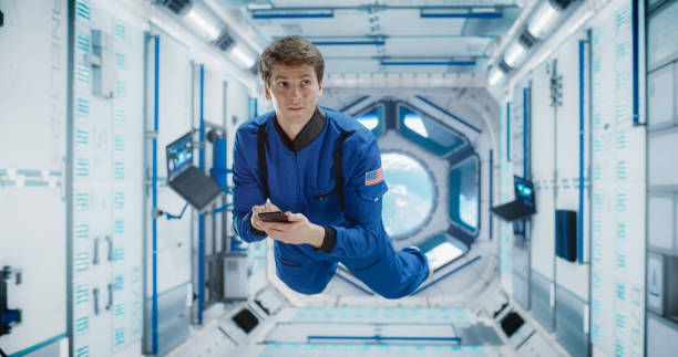 istock Cheerful Male Astronaut Floating in Zero Gravity Inside a Spaceship. Happy Caucasian Specialist Using Smartphone in Space, Checking News, and Communicating with Family and Friends Online. 2156520247