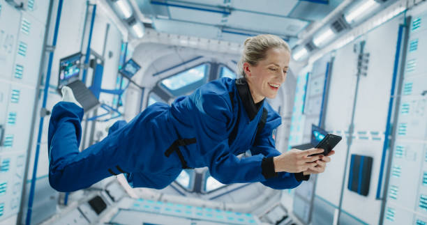 istock Cheerful Female Astronaut Floating in Zero Gravity Inside a Spaceship. Happy Caucasian Specialist Using Smartphone in Space, Checking News, and Communicating with Family and Friends Online. 2156520281
