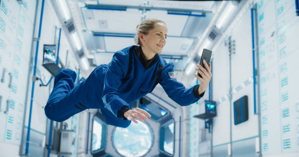 istock Cheerful Female Astronaut Floating in Zero Gravity Inside a Spaceship. Happy Caucasian Specialist Using Smartphone in Space, Checking News and Communicating with Family or Friends Online. 2156520310
