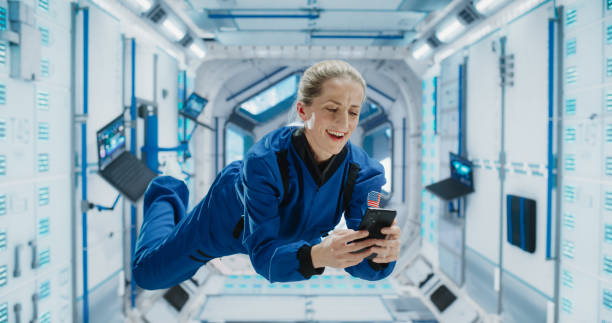 istock Cheerful Female Astronaut Floating in Zero Gravity Inside a Spaceship. Happy Caucasian Specialist Using Smartphone in Space, Checking News and Communicating with Family and Friends Online. 2156520326