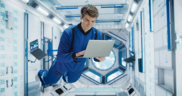 Caucasian Male Astronaut Using a Laptop to Wirelessly Connect to a Satellite. Scientist Working on Computer Device Inside an Intergalactic Station. Professional Engineer Undertaking Online Service Job
