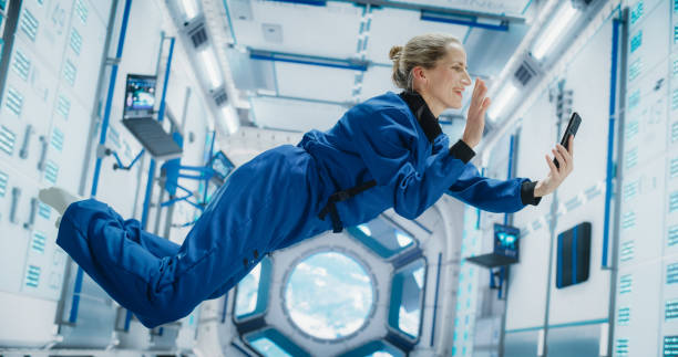 istock Astronaut Floating in Zero Gravity on Board a Spacecraft. Female Having a Video Call with a Family or Friends From Planet Earth. Engineer Using Smartphone in Space Inside an Orbiting Spaceship 2156520659