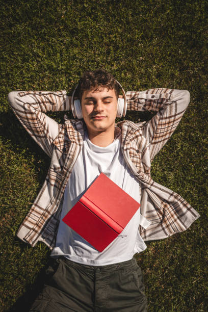 istock Young boy with headphones and book lying down on the grass 2156521277