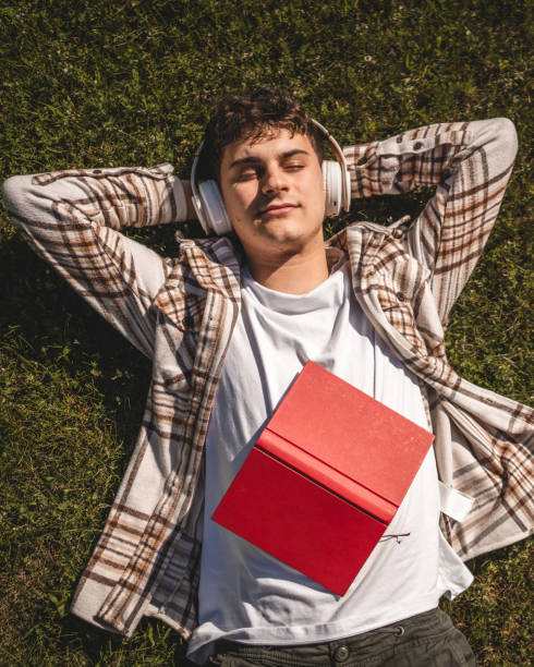 istock Young boy with headphones and book lying down on the grass 2156522166