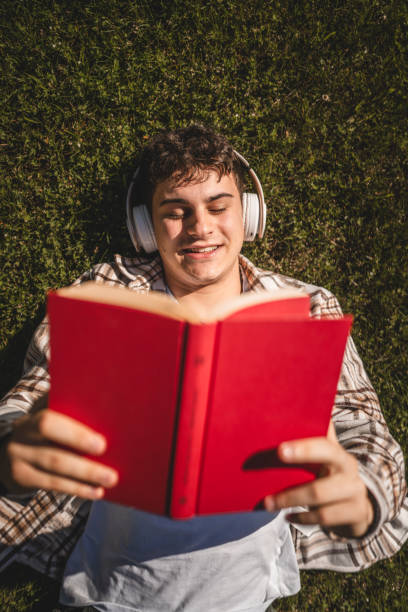 istock Young boy with headphones lying down on the grass and read a book 2156522282