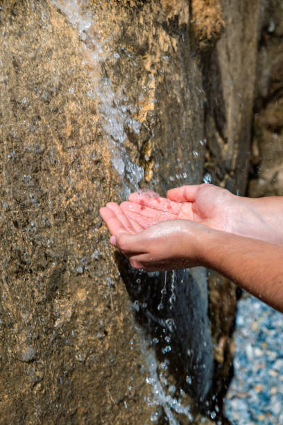 Hands together, in the foreground, taking water from a small waterfall, feeling of freshness.