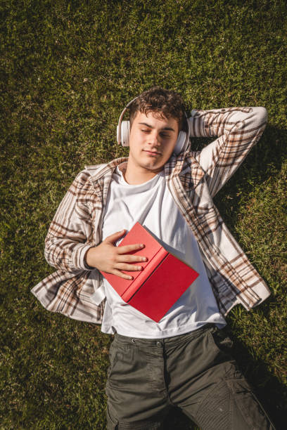 istock Young boy with headphones and book lying down on the grass 2156523099