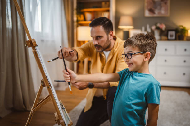 istock Father teach mentor son to create art at home on easel with brush 2156523178