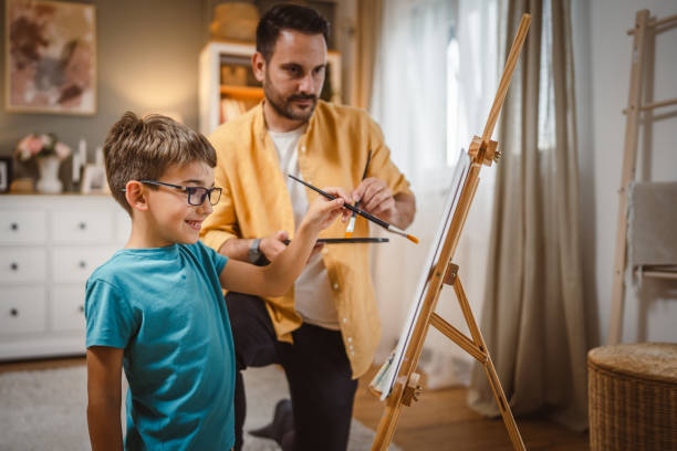 istock Father teach mentor son to create art at home on easel with brush 2156523594