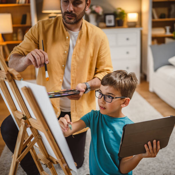 istock Father mentor teach son to paint at home while son hold tablet 2156523709