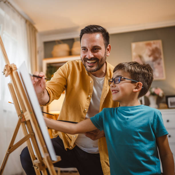 istock Father teach mentor son to create art at home on easel with brush 2156523980