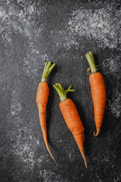 istock 3 three organic carrots over dark textured background with space for text 2156526729