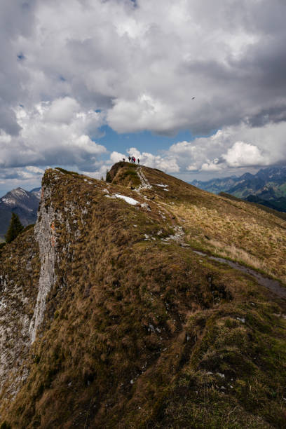 A small group of people on top of the mountain with clouds in the background