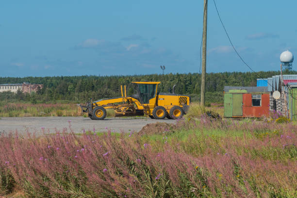 Large yellow grader machinery smoothing and flattening roadbed, preparing base layer for new asphalt pavement, essential step in modern roadway infrastructure and street improvement works.