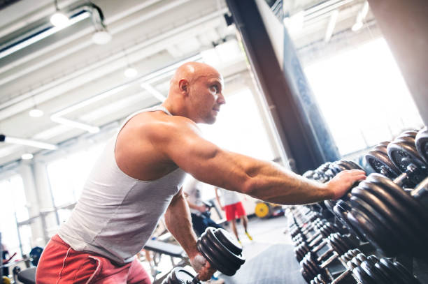 istock Close up of man performing single arm dumbbell row in bent-over position. Routine workout for physical and mental health. 2156547329