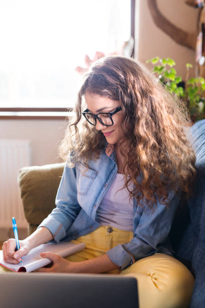 istock A beautiful university student having online class, e-learning sitting at home on the couch, laptop on knees. 2156548639