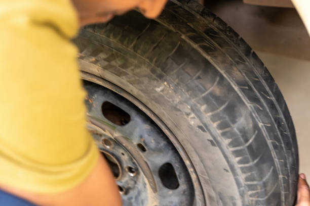 A mechanic wearing blue and black gloves tightens a red wheel hub with a wrench in a workshop setting. The image captures hands, tools, and the vehicle wheel, conveying mechanical work, maintenance, and industrial precision. Warm tones emphasize the red hub and the focus on assembly activity.