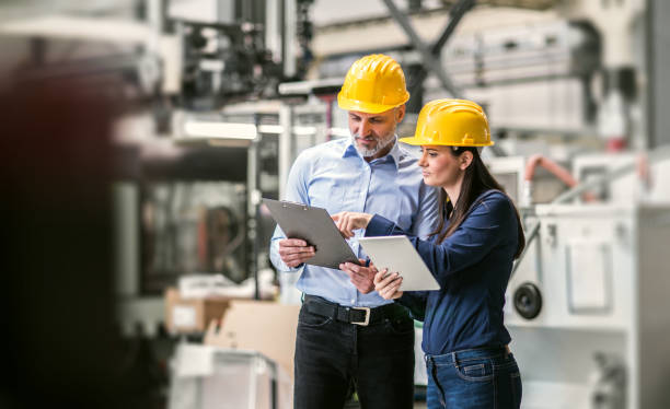 istock Two project managers standing in modern industrial factory. Manufacturing facility with robotics, robotic arms and automation. Storing products and materials in warehouse. 2156551472