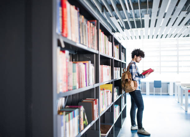 istock Male student in library, looking for books, preparing for final exam. 2156552383
