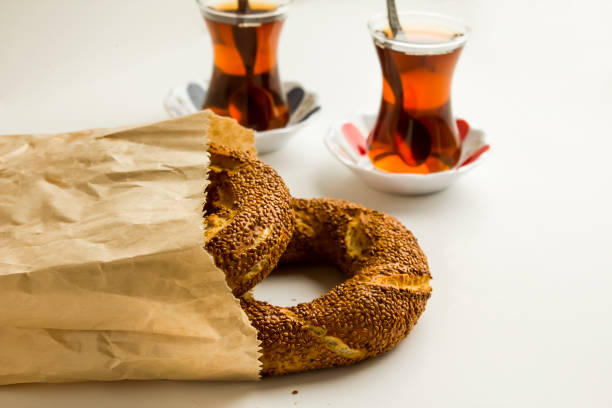 Close-up taken of Traditional Turkish sesame bagel, simit, in paper bag with traditional Turkish Tea and cheese on white background