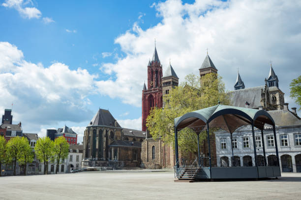 The grandeur of a red-stone Saint Jean church, Sintservaas basilic, age-old structures defines the perimeter of a broad plaza, set against the dramatic backdrop of a cloud-speckled azure sky
