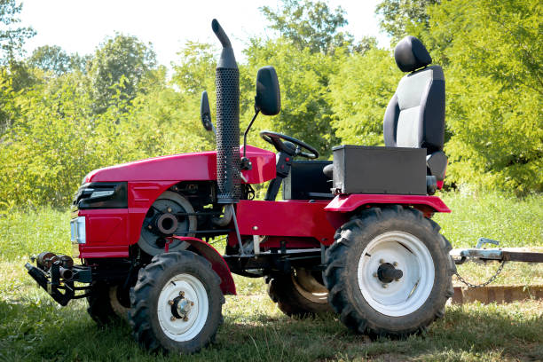 Small mini red modern new tractor standing at farm, field, nature countryside during sunny summer day close up. Small agricultural machinery. Rural country farmland background.