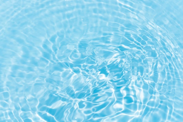 Blue water with ripples on the surface. Defocus blurred transparent blue colored clear calm water surface texture with splashes and bubbles. Water waves with shining pattern texture background.