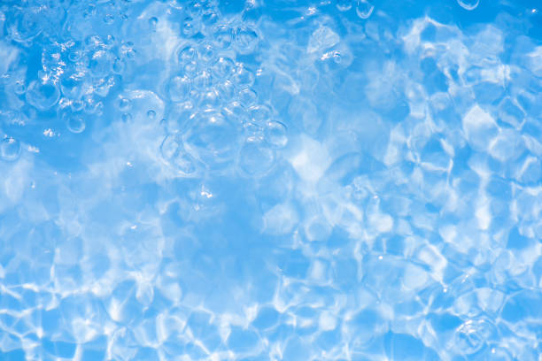 Blue water with ripples on the surface. Defocus blurred transparent blue colored clear calm water surface texture with splashes and bubbles. Water waves with shining pattern texture background.