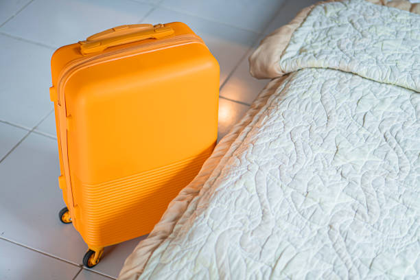 istock Yellow suitcase next to bed with white quilted blanket 2156567251