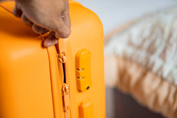 istock Person zipping an orange suitcase with built-in lock 2156567319