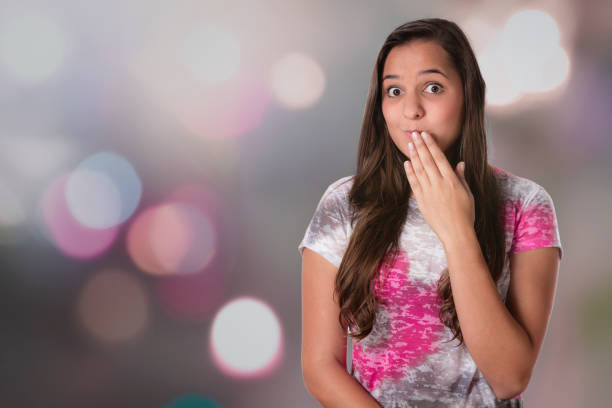 Facial expressions themes: Embarrassed surprised Hispanic young woman with hand covering mouth. Waist up shot with model feeling embarrassed while looking at camera.
