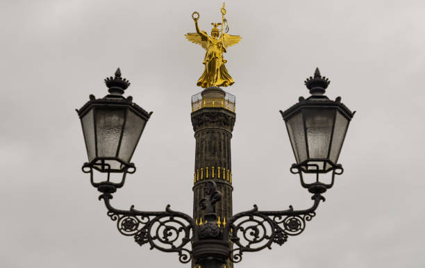 Berlin, Germany - Dec 20, 2023 - Street lamppost with The victory column in the background. Upper part of the Victory column with Goddess Victoria to Celebrate Prussia's victory in the Franco-German War in the Tiergarten. Space for text, Selective focus.