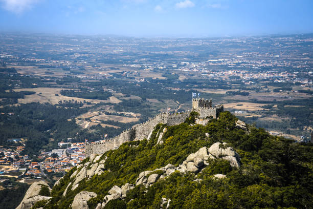 Panoramic view from the ancient walls of the Moorish Castle in Sintra, Portugal, overlooking the lush green landscape with Pena Palace visible in the distance.