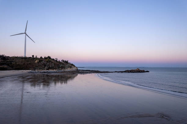 istock Beach and waves along the dusk coastline, and wind turbines on small mountain 2156573043