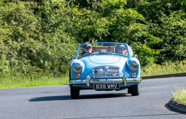 Stony Stratford,UK - June 2nd 2024: 1959 bright blue MG A classic British sports car driving on a British country road.Picnic basket on boot.