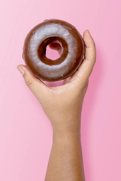 A human hand holding a delicious donut with a chocolate sprinkle decoration