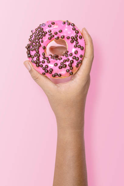 istock Hand holding a pink sprinkled donut against pastel background 2156581539