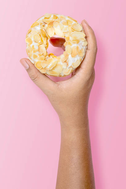 Hand holding a white almond donut on pink background