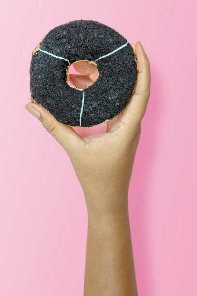 istock Hand holding black charcoal donut on pink background 2156581591