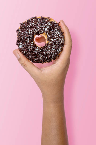 istock Hand holding chocolate sprinkle donut on pink background 2156581592