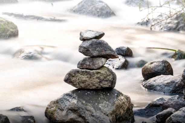 A stack of rocks is on top of a river. The rocks are large and the water is calm. The scene is peaceful and serene in Grojogan Watu Purbo, Yogyakarta, Indonesia