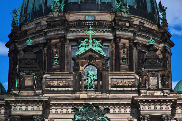 A view of the Berlin Cathedral's green dome and the historic bridge over the River Spree in Berlin, Germany, under a clear blue sky. The scene captures the essence of Berlin's architectural heritage.