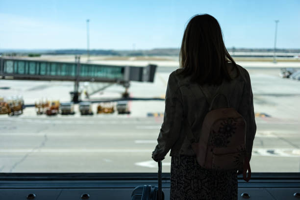 istock Woman with her back turned looking out the window while waiting to catch the flight that is delayed. 2156593631