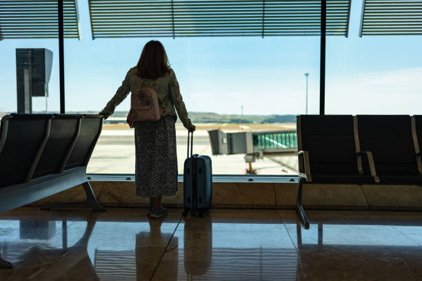 istock Woman with her back turned looking out the window while waiting to catch the flight that is delayed. 2156593633