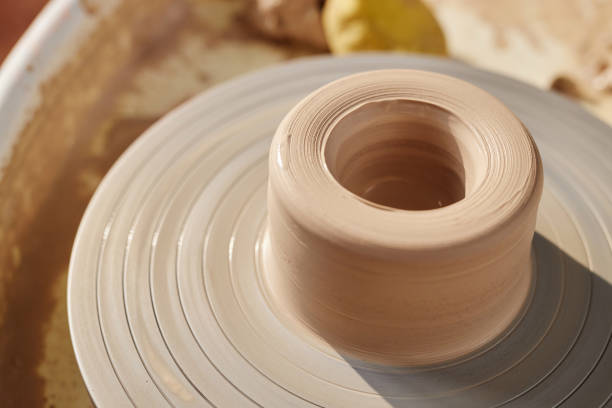 Minimal close up of carefully shaped raw clay on pottery wheel lit by sunlight copy space
