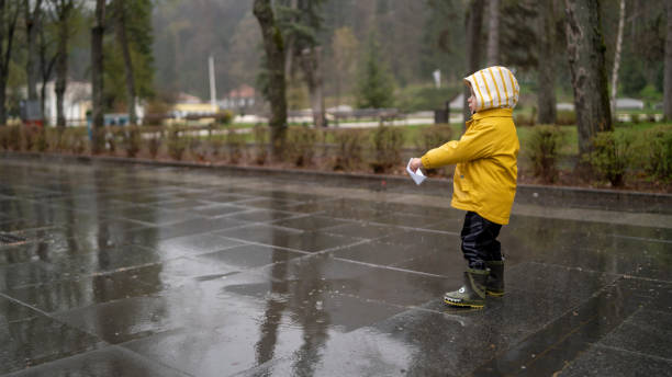 istock It's springtime. A small child in rubber boots jumps through puddles, plays and launches paper boats on the water. 2156606069