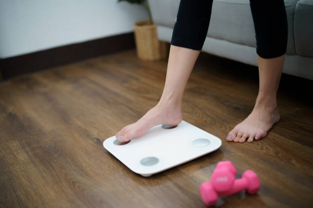 istock Fat diet and scale feet standing on electronic scales for weight control. Measurement instrument in kilogram for a diet control 2156606847