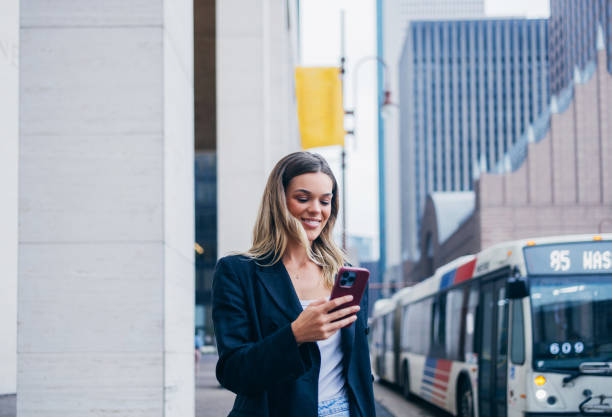 istock Smiling Woman Using Smartphone At City Bus Stop 2156614215